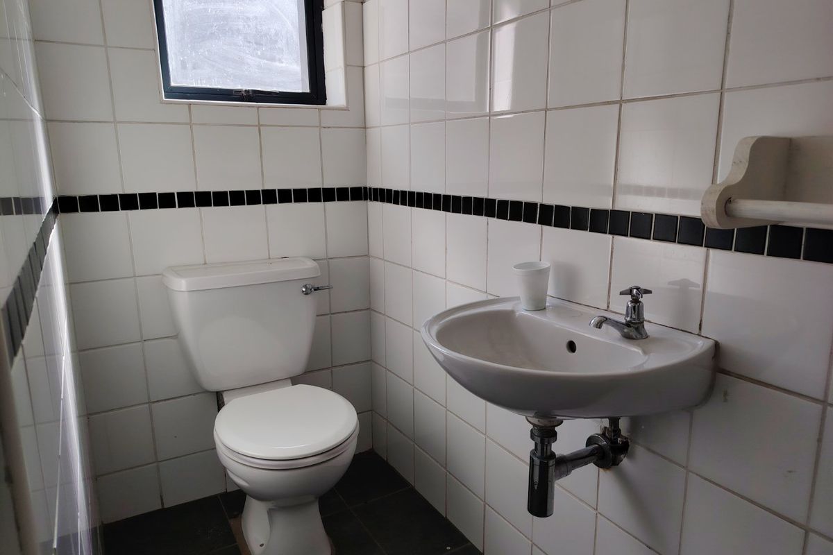A functional industrial-style bathroom featuring a wall-mounted basin, toilet, and classic white ceramic wall tiles with a black accent border.