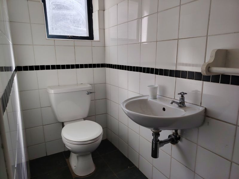 A functional industrial-style bathroom featuring a wall-mounted basin, toilet, and classic white ceramic wall tiles with a black accent border.