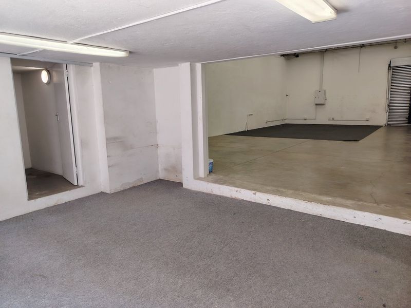 An open-plan industrial utility space featuring concrete flooring, fluorescent lighting, and a roller shutter door, suitable for storage or workshop use.