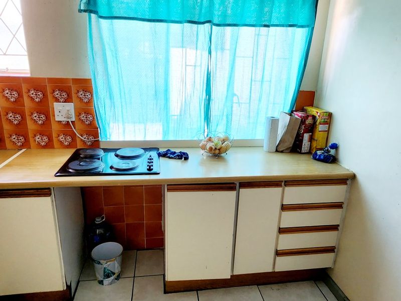 A compact kitchen featuring a built-in electric hob, laminate countertops, tiled splashbacks, and functional cabinetry with ceramic floor tiles.