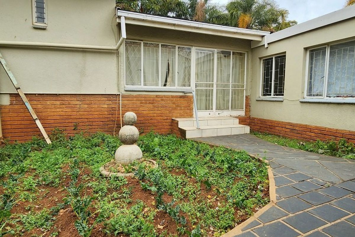 Rear exterior view of the apartment featuring a paved walkway, brick facade, and an overgrown garden area requiring maintenance.