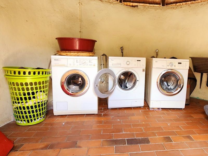 A functional laundry area featuring terracotta tile flooring, a traditional thatch roof, and multiple appliance connections with a wall-mounted sink.