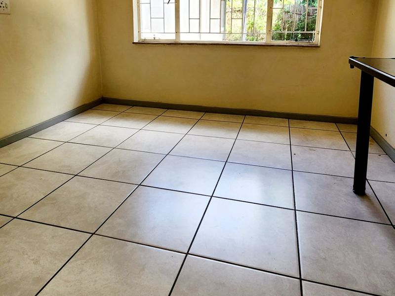 An empty bedroom featuring tiled flooring and a window with security bars, showing signs of ceiling water damage and dated wall finishes.