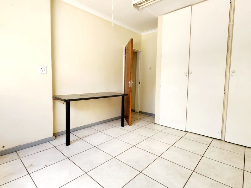 A vacant bedroom featuring white built-in cupboards, tiled flooring, and neutral wall finishes, offering a blank canvas for potential renovation or restyling.