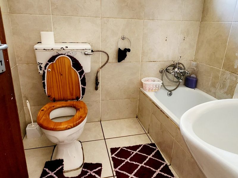 A functional bathroom featuring a bathtub, pedestal basin, and toilet, finished with ceramic tiling and security bars on the windows.