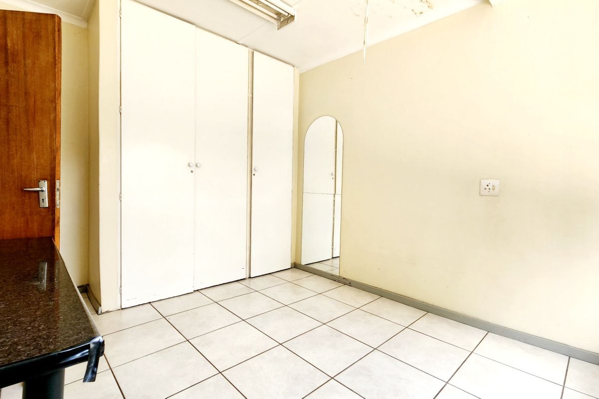 An empty bedroom featuring tiled flooring and built-in cupboards, requiring minor ceiling repairs and cosmetic updates.