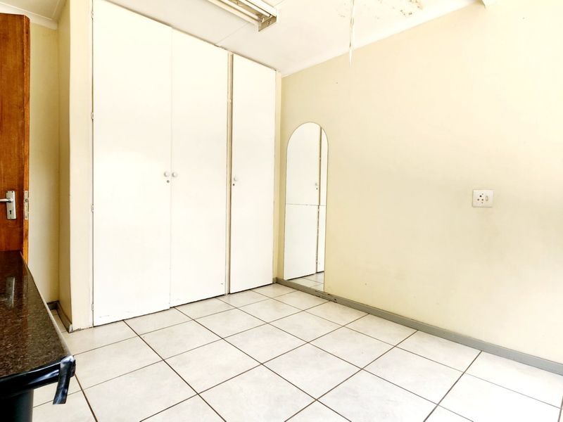 An empty bedroom featuring tiled flooring and built-in cupboards, requiring minor ceiling repairs and cosmetic updates.