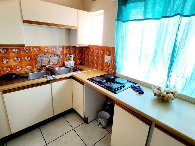 A compact kitchen featuring laminate countertops, built-in cabinetry, a double bowl stainless steel sink, and an integrated electric hob with dated wall tiling.
