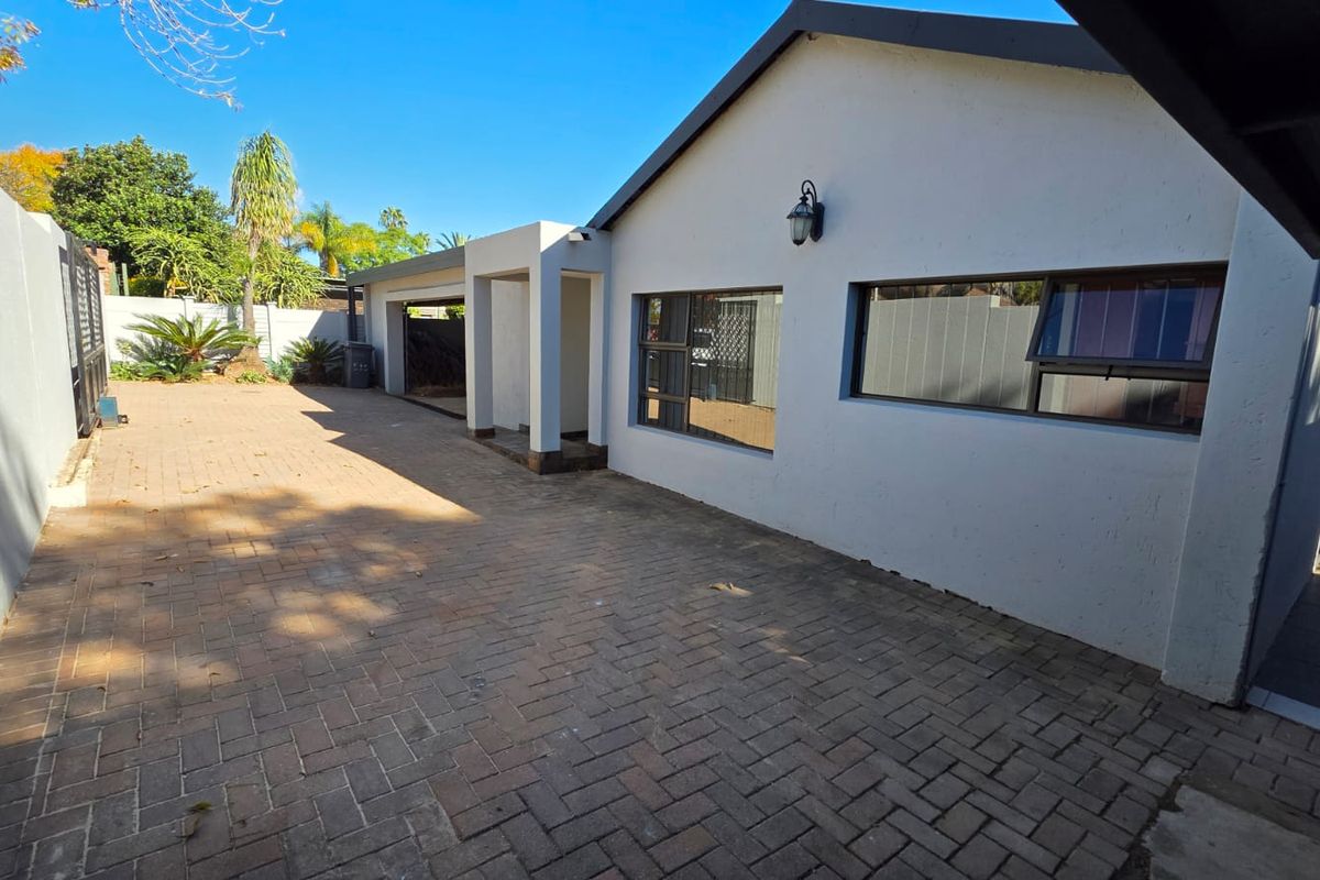 A paved rear courtyard area featuring a clean exterior facade, aluminium window frames with security bars, and a covered entrance.