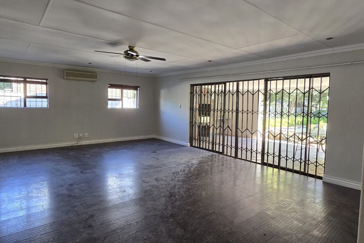 Spacious, empty living room featuring laminate flooring, a ceiling fan, split-system air conditioning, and large sliding glass doors with security gates leading outdoors.