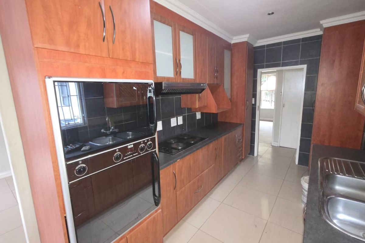 A functional kitchen featuring wood-finish cabinetry, built-in oven and hob, extractor fan, and double stainless steel sink with tiled splashbacks.