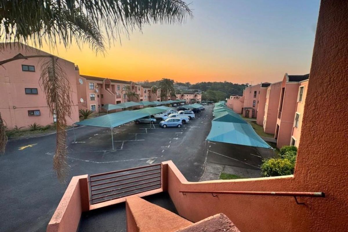 Elevated view of the apartment complex parking area featuring covered parking bays and access staircases at sunset.