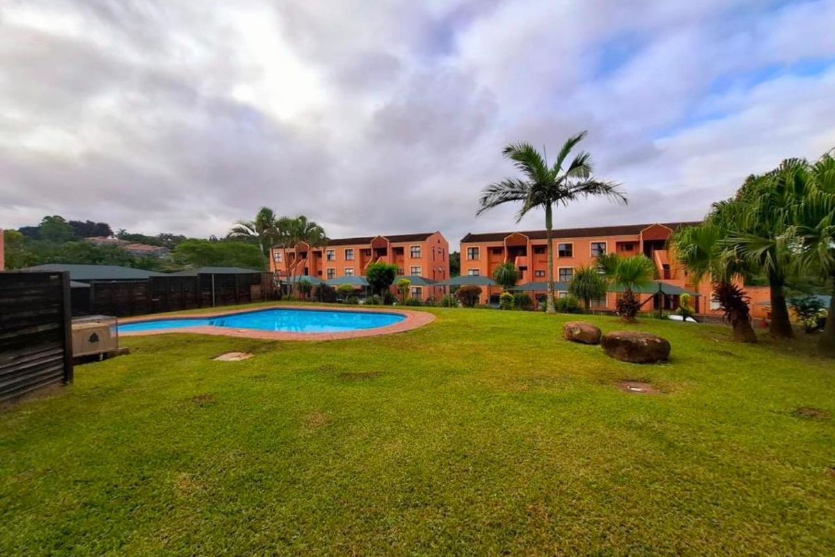 Communal outdoor area featuring a swimming pool set within a well-maintained garden, serving the apartment complex.