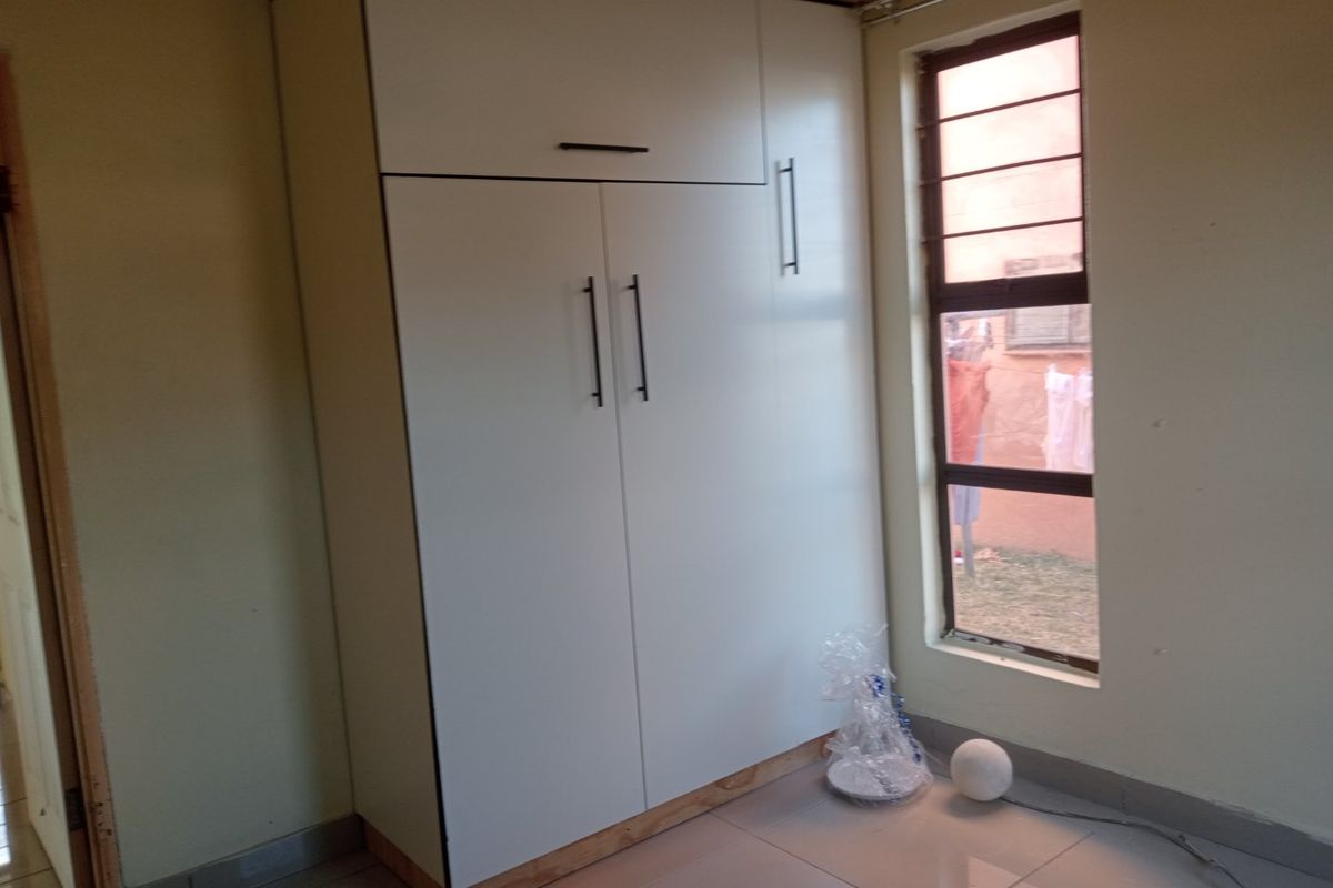 A bedroom featuring a modern white built-in wardrobe, tiled flooring, and a window fitted with security burglar bars.