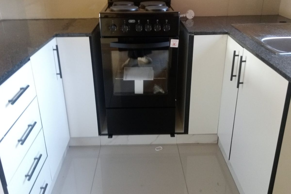 A compact kitchen featuring white cabinetry, dark granite countertops, a stainless steel sink, and a freestanding stove with ceramic tiled flooring.