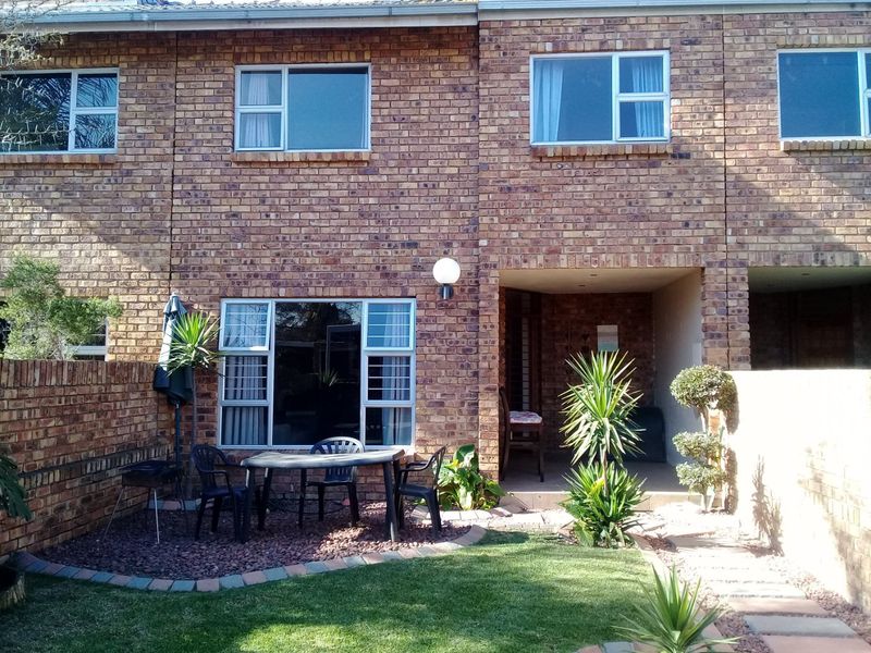 Rear view of a face brick townhouse featuring a covered patio area, small garden, and paved walkway.
