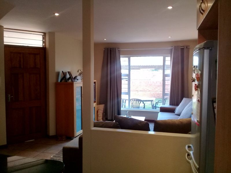 A view from the kitchen into the living area, featuring tiled floors, recessed lighting, and a large window providing natural light and garden access.