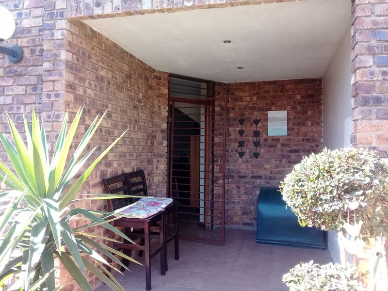 A covered patio area featuring exposed brick walls, tiled flooring, and a secure metal entrance gate, providing a functional outdoor transition space.