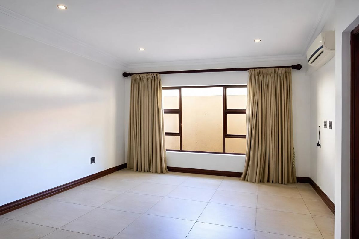 A spacious, empty bedroom featuring neutral tiled flooring, recessed downlighting, and a wall-mounted air conditioning unit, offering a clean and versatile living space.