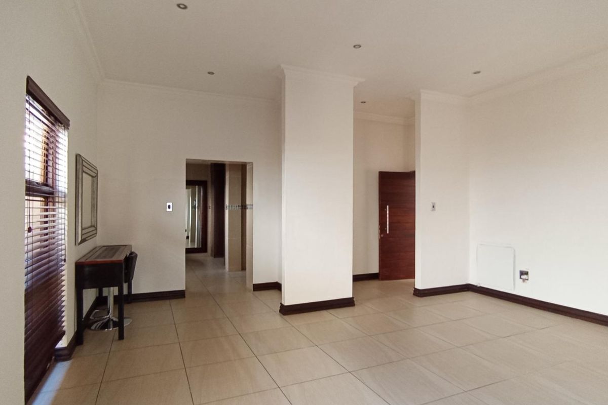 A spacious, neutral living area featuring large format floor tiles, recessed lighting, and clean white walls, offering a versatile blank canvas.