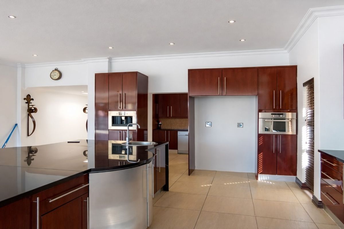 Modern kitchen featuring dark wood cabinetry, black granite countertops, a stainless steel island, and integrated appliances, with an adjacent scullery area.