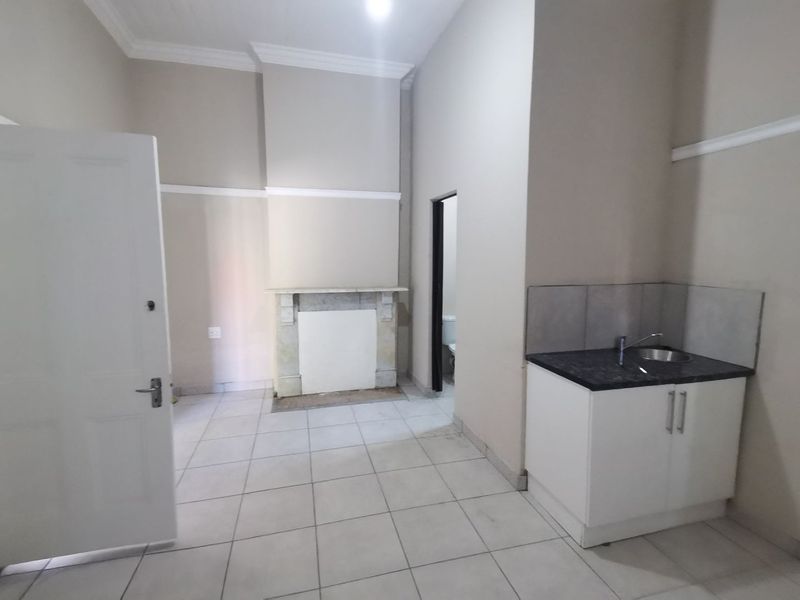 Open plan living area featuring a fireplace, kitchenette with sink, tiled flooring, and crown molding, presenting a blank canvas for potential updates.