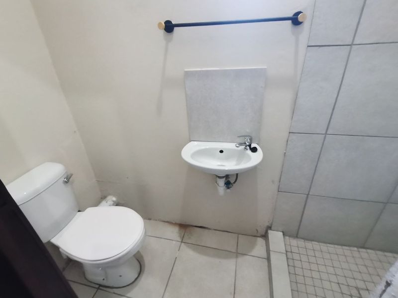 A compact bathroom featuring a wall-mounted basin, toilet, and a tiled shower area, requiring minor cosmetic updates to improve its overall condition.