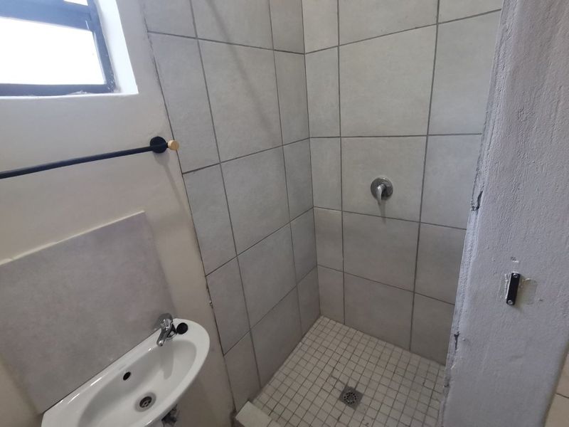 A compact bathroom featuring a tiled shower enclosure and a wall-mounted basin, requiring some cosmetic updates to the wall finishes.