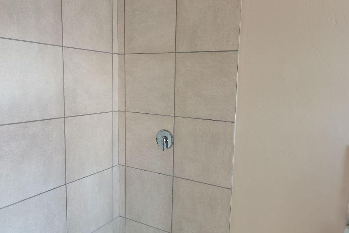 A clean, modern shower enclosure featuring neutral-toned ceramic wall tiles and chrome fixtures.