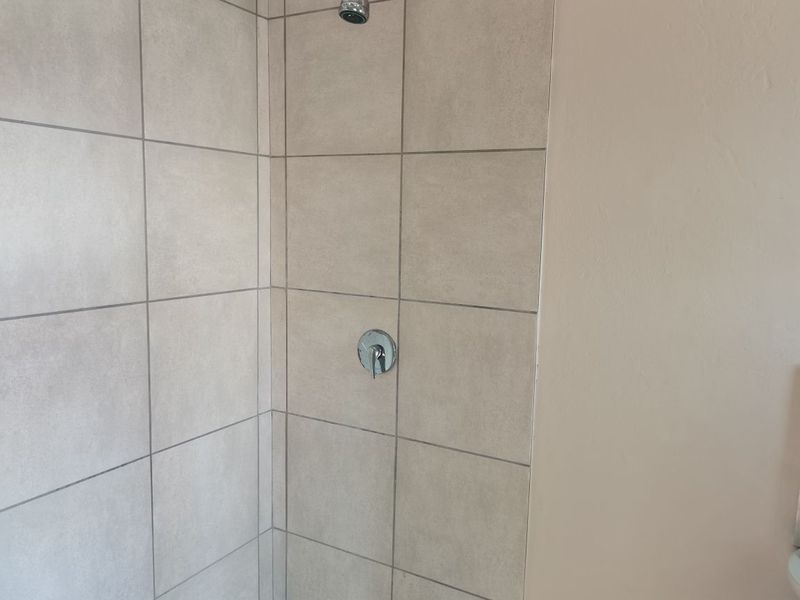 A clean, modern shower enclosure featuring neutral-toned ceramic wall tiles and chrome fixtures.