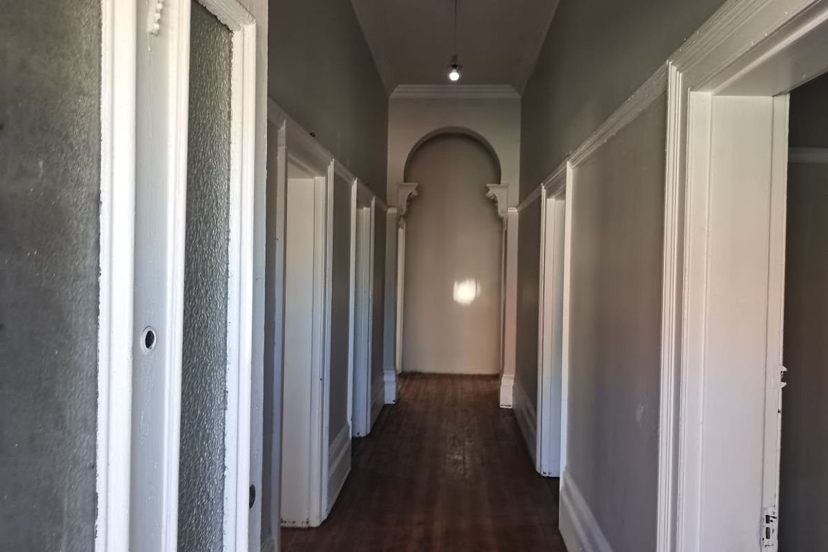 A long, empty hallway featuring traditional architectural details including an archway, ceiling rose, and timber flooring, presenting a classic character aesthetic.