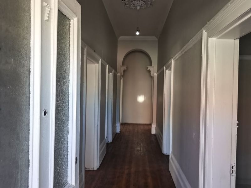 A long, empty hallway featuring traditional architectural details including an archway, ceiling rose, and timber flooring, presenting a classic character aesthetic.