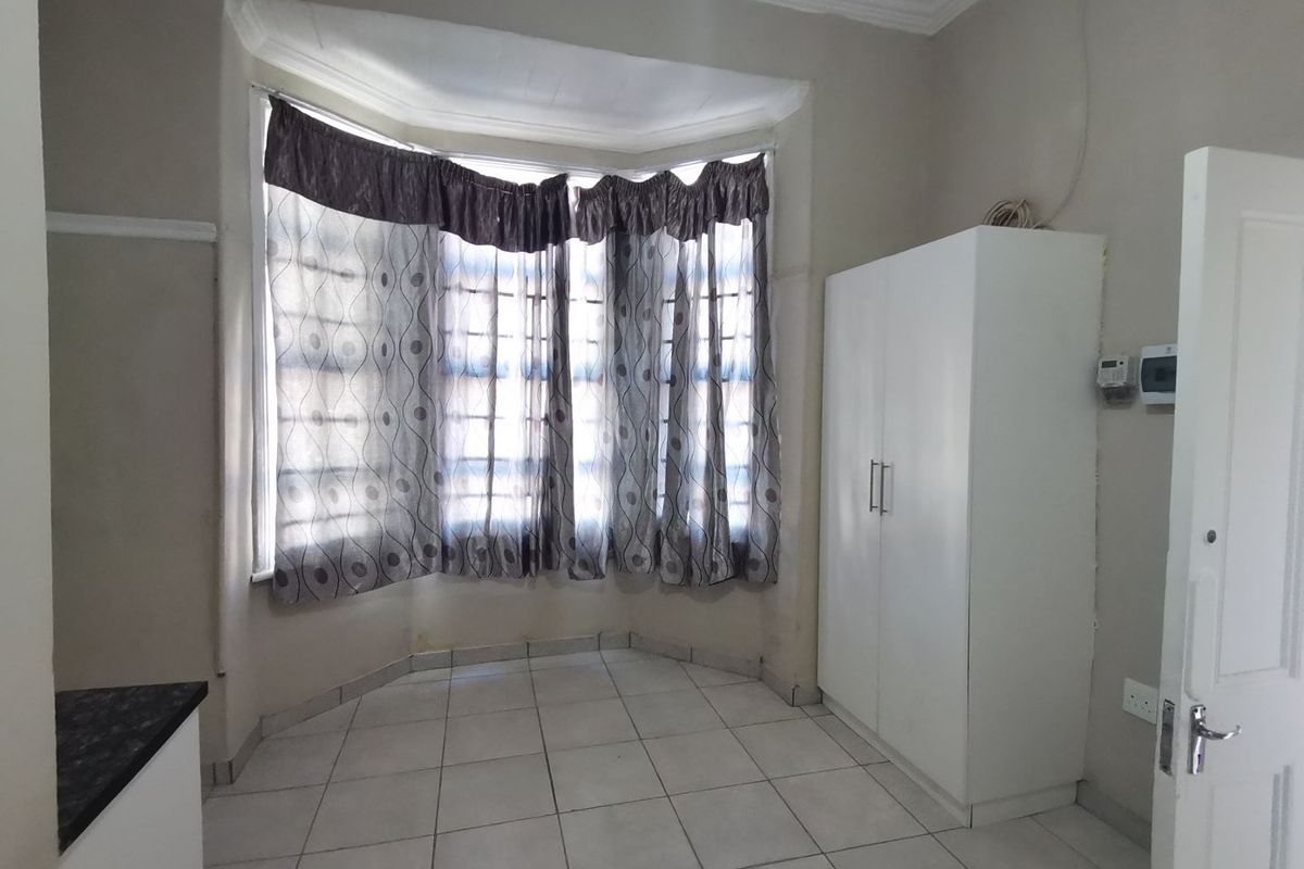 A bedroom featuring a bay window, tiled flooring, and a built-in wardrobe, offering a functional space with potential for cosmetic updates.