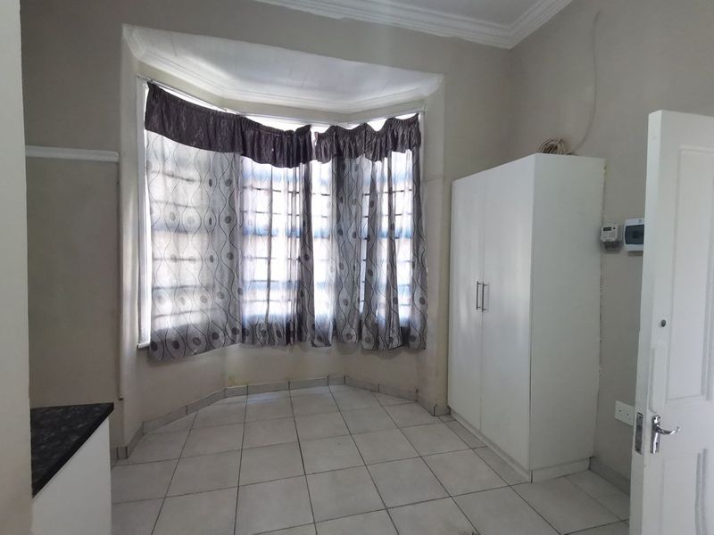 A bedroom featuring a bay window, tiled flooring, and a built-in wardrobe, offering a functional space with potential for cosmetic updates.