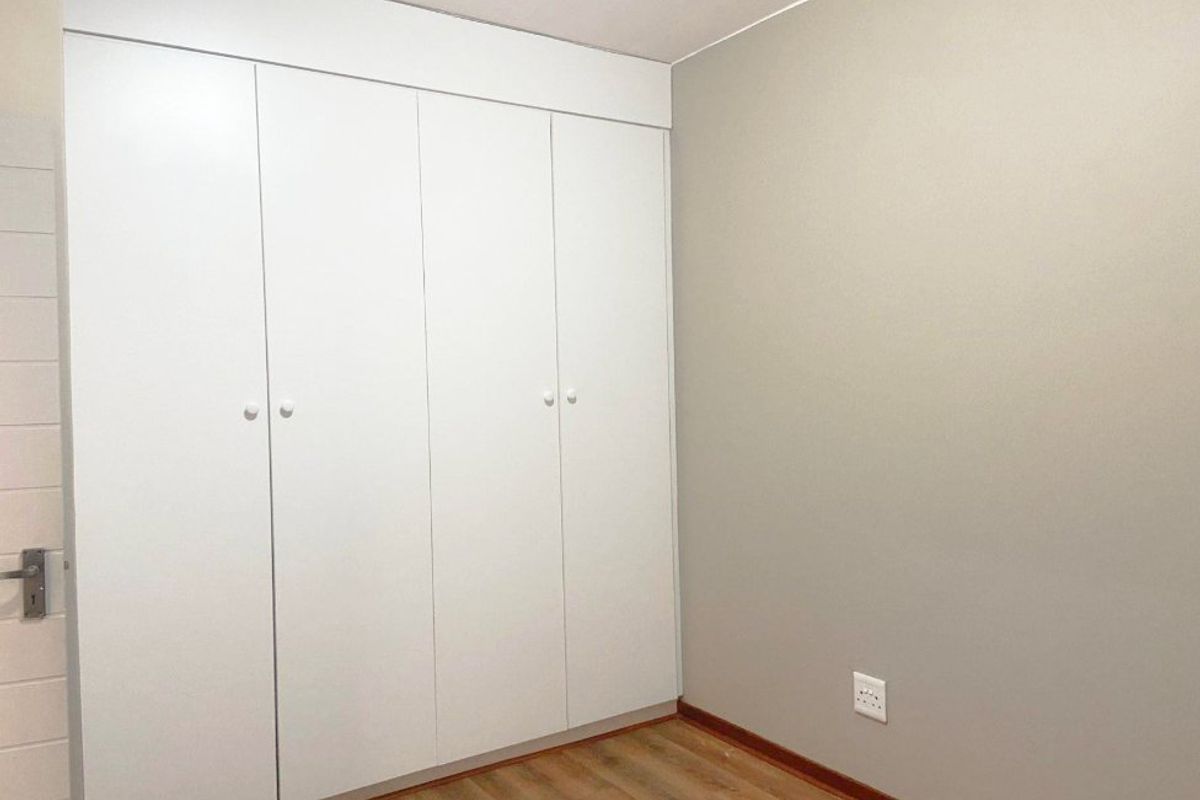A clean, empty bedroom featuring neutral walls, laminate flooring, and ample built-in cupboard storage space.