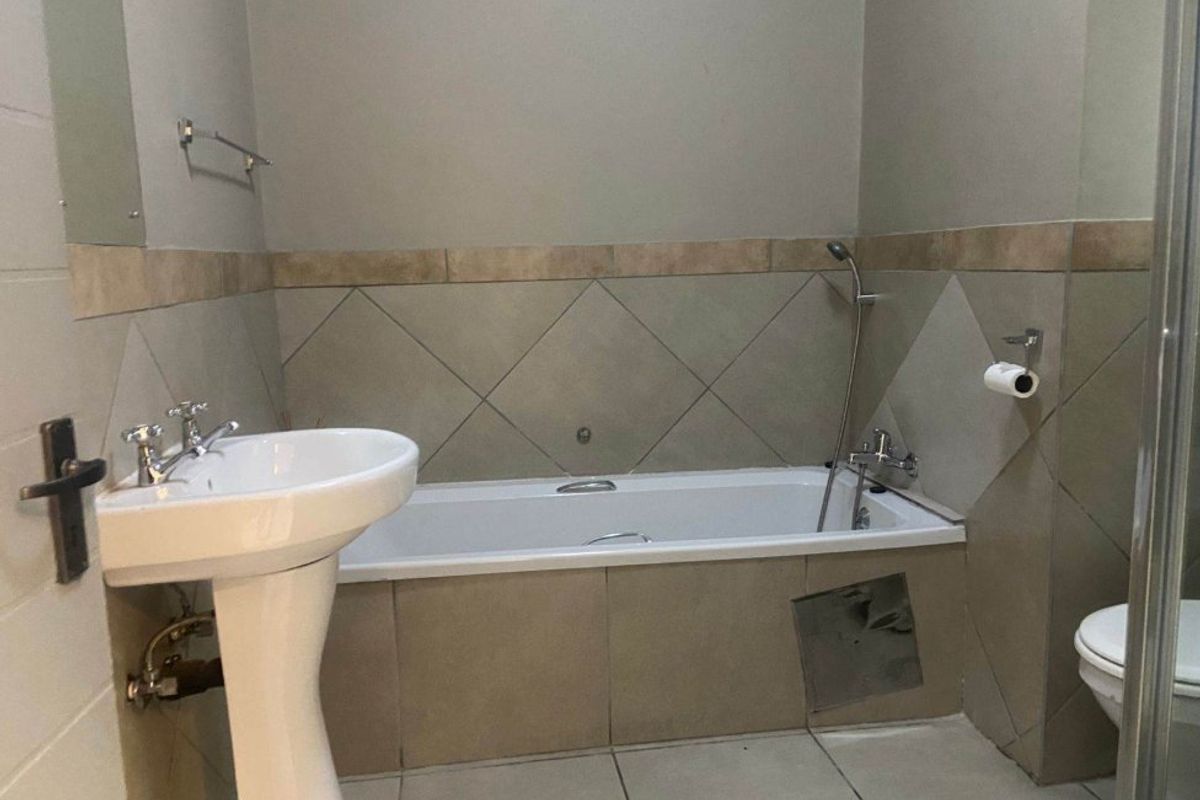 A functional bathroom featuring a pedestal basin, built-in bathtub with handheld shower mixer, and tiled finishes throughout.