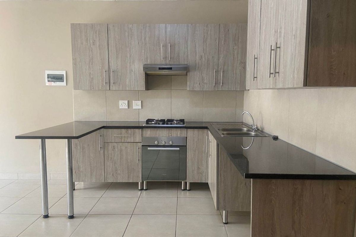 Modern kitchen featuring light wood-grain cabinetry, dark granite countertops, built-in gas hob, oven, extractor fan, and double sink with tiled flooring.