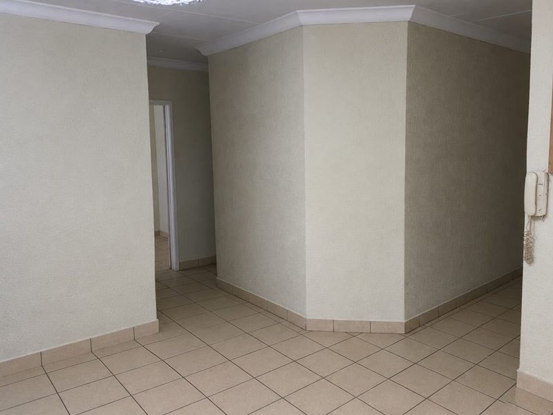 A clean, empty hallway featuring neutral tiled flooring, coved cornicing, and a wall-mounted intercom system, providing access to adjacent rooms.