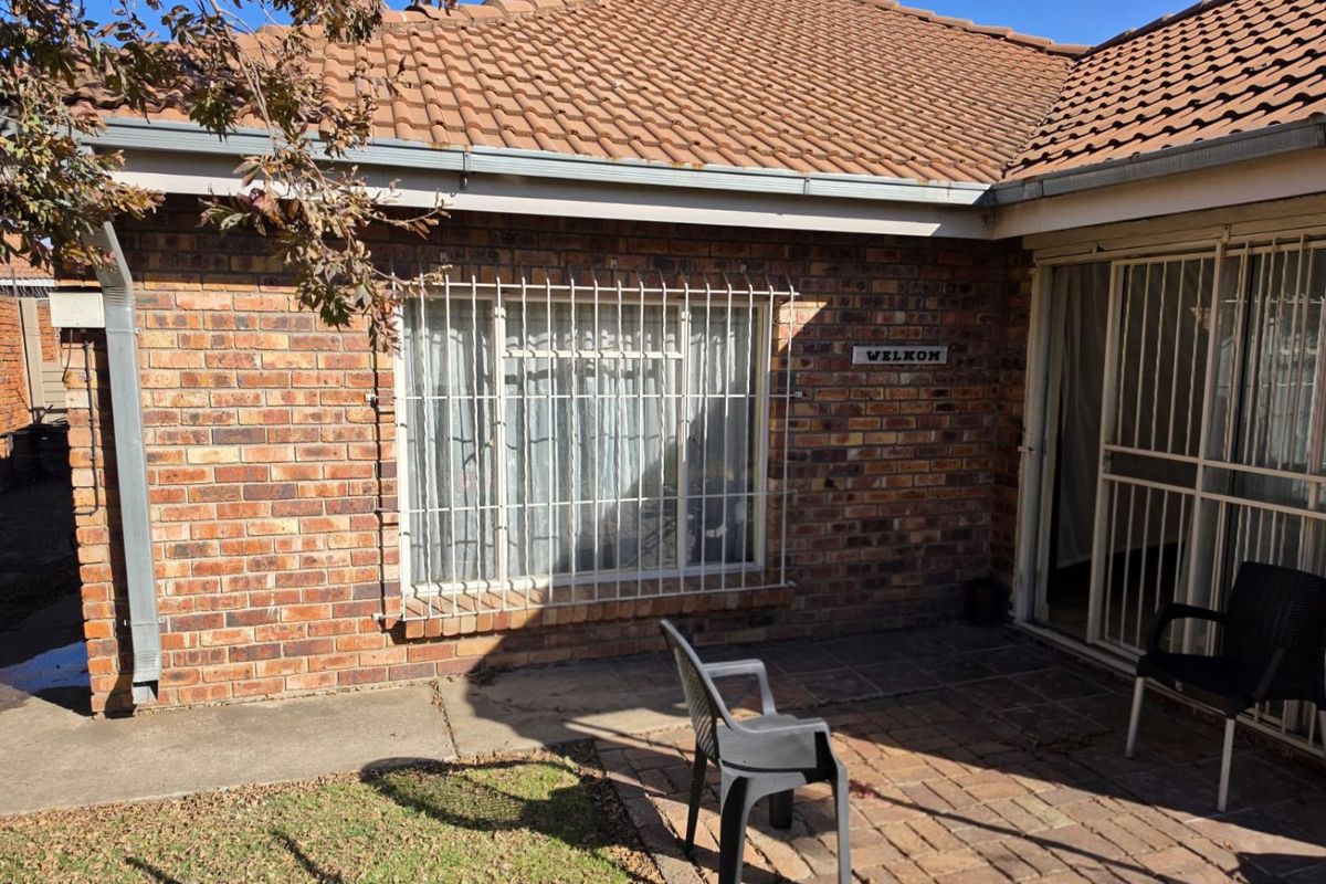Rear exterior view of the apartment featuring a face brick facade, tiled roof, paved patio area, and security bars on windows and doors.
