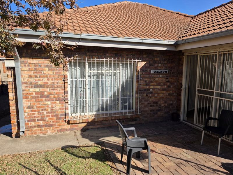 Rear exterior view of the apartment featuring a face brick facade, tiled roof, paved patio area, and security bars on windows and doors.