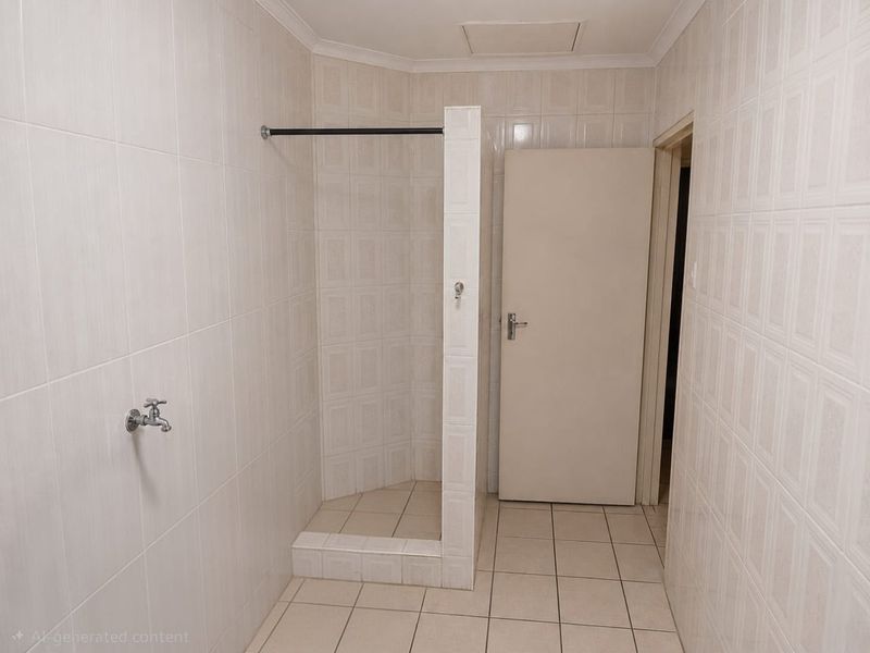 A functional, fully tiled bathroom featuring a walk-in shower cubicle and neutral finishes, ready for modern updates.