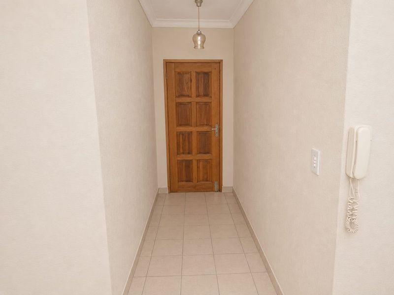 A clean and well-maintained hallway featuring neutral tiled flooring, a solid timber door, and a wall-mounted intercom system.