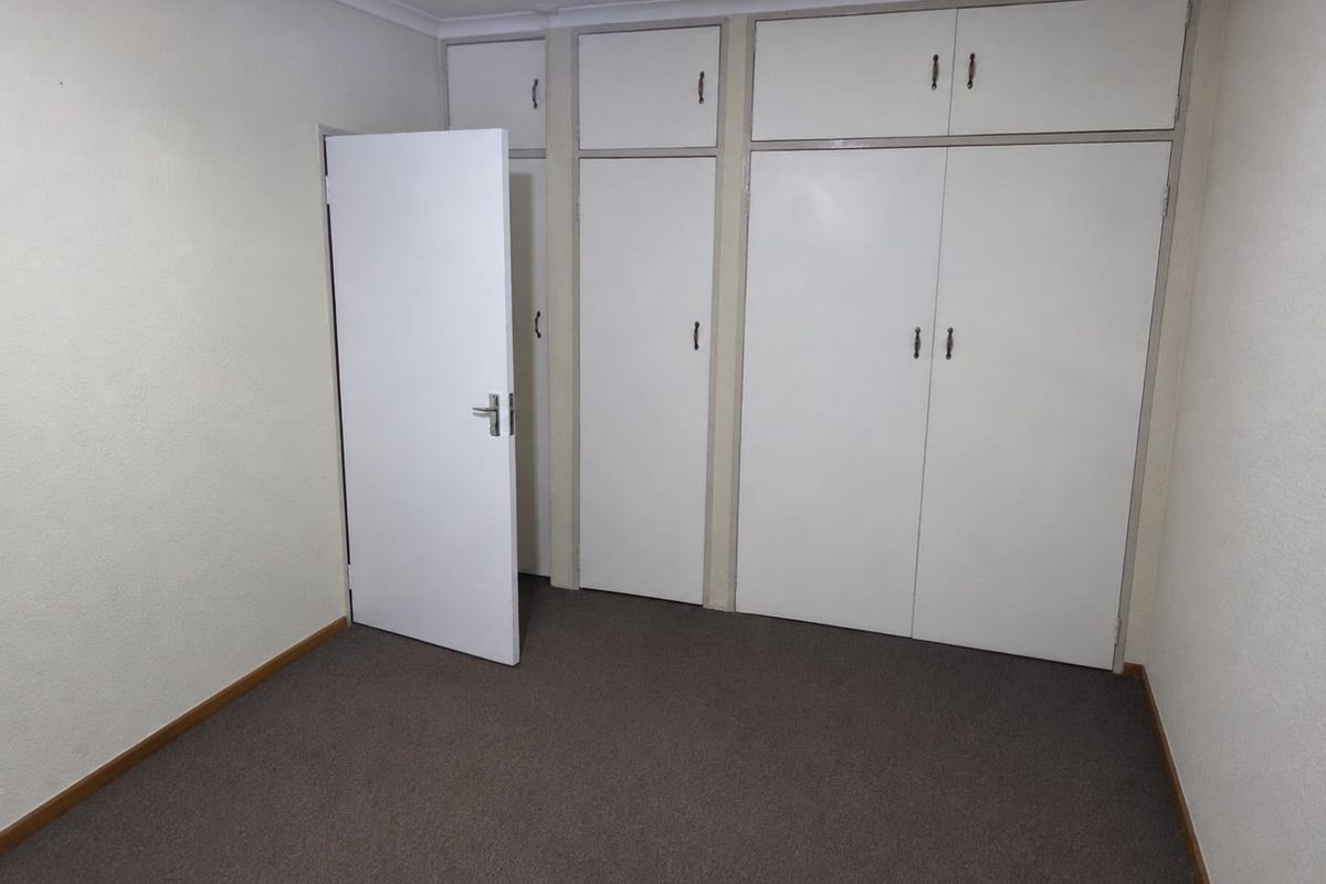 An empty bedroom featuring neutral walls, carpeted flooring, and extensive built-in cupboard storage with overhead cabinets.