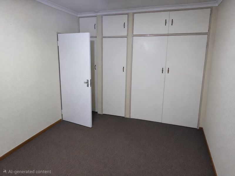 An empty bedroom featuring neutral walls, carpeted flooring, and extensive built-in cupboard storage with overhead cabinets.