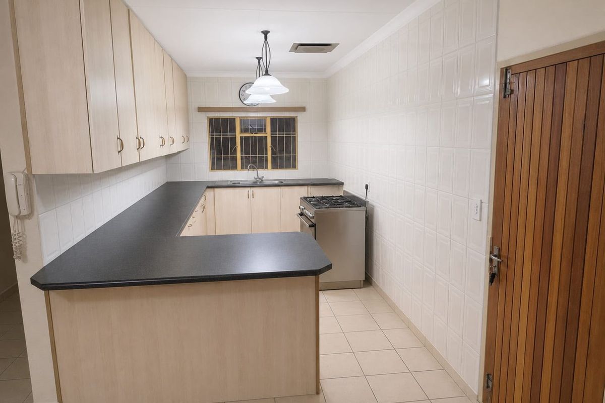 A clean, functional kitchen featuring light wood-finish cabinetry, dark laminate countertops, tiled splashbacks, and a gas stove, offering a practical layout.