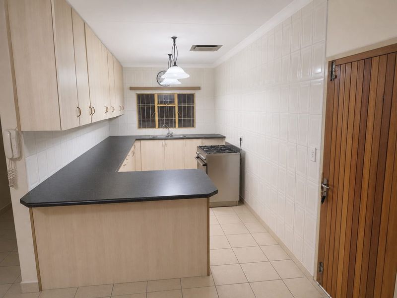 A clean, functional kitchen featuring light wood-finish cabinetry, dark laminate countertops, tiled splashbacks, and a gas stove, offering a practical layout.