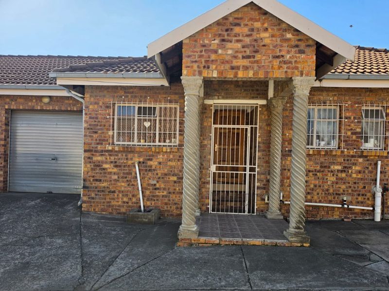 Front elevation of a face brick apartment featuring a covered entrance with decorative columns, security gates, and an integrated roller shutter garage.
