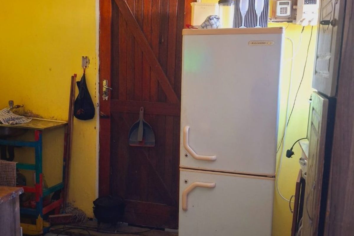 A dated kitchen area featuring checkered floor tiles, a timber door, and exposed electrical wiring on yellow walls.