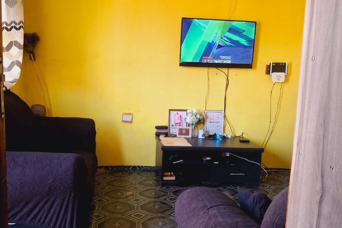 A living room featuring patterned floor tiles and a wall-mounted television, requiring cosmetic updates to improve the overall aesthetic and finish.