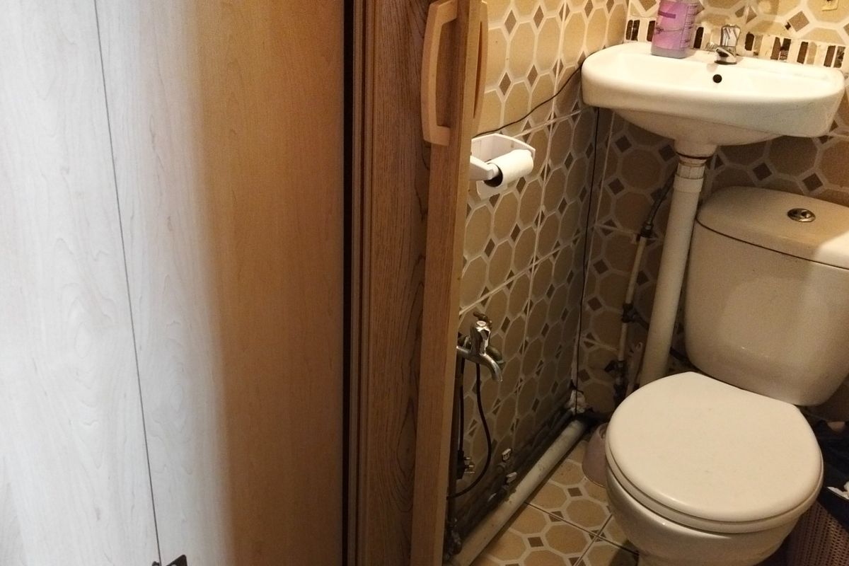 A compact bathroom featuring a pedestal sink, toilet, and dated ceramic tiling with exposed plumbing fixtures.